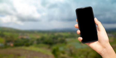 beautiful female hand holding smart phone with black screen against nature moutain with clound background, technology and nature concept. banner and copy spaceの写真素材