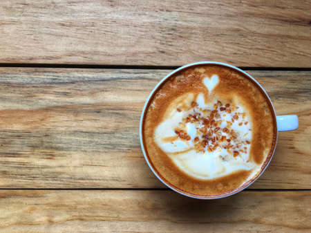 Hot cappuccino coffee in white cup with brown cane sugar topping on wooden table background. Art of...