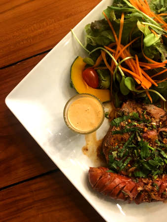 Pork steak and sausage with spicy herbal sauce and salad with dressing in plate put on wooden table backgroundの写真素材