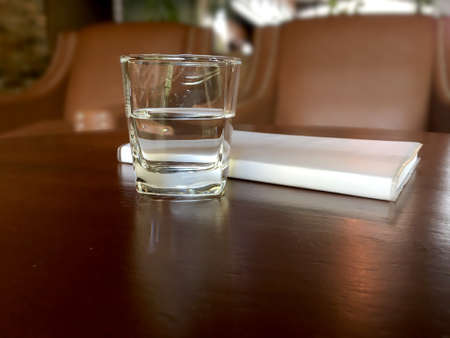 Mineral drink water in transparent glass with notebook on brown wooden table in the cafe.