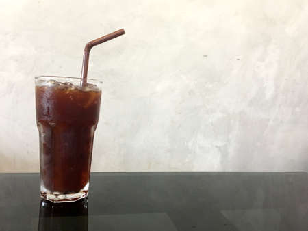 Ice black coffee in transparent glass with brown tube on glass table in the cafeの写真素材