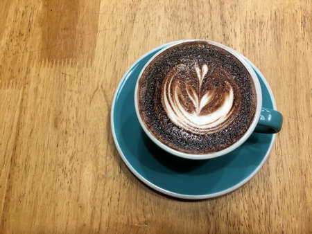 Hot dark chocolate in blue cup on wooden table background. Art of milk foam drawing like white leaf on dark brown melt chocolate top view.の写真素材