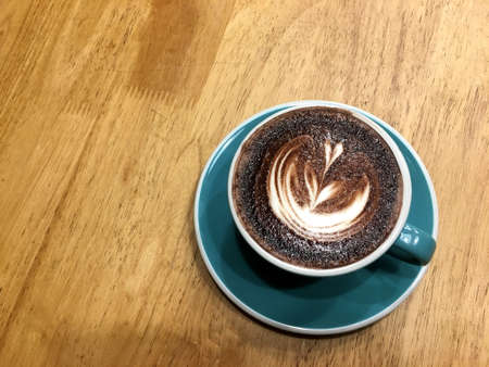 Hot dark chocolate in blue cup on wooden table background. Art of milk foam drawing like white leaf on dark brown melt chocolate top view.の写真素材
