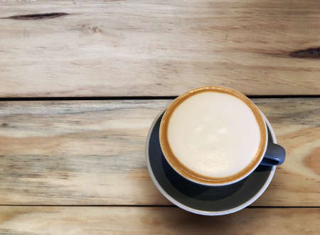 Hot cappuccino coffee in blue cup on wooden table background. Art of milk foam circle shape with...