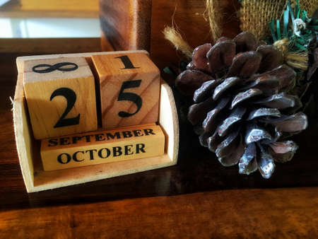 Wood block vintage calendar showing the date of 25th October beside dry pine nut cone on wooden...