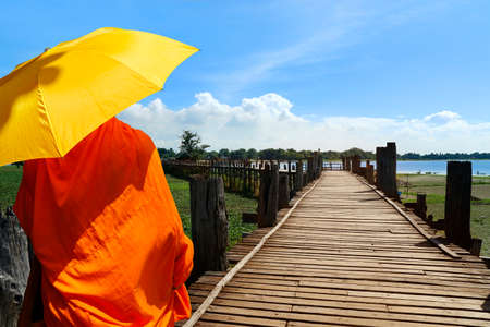 monk with umbrella, walking on a bath bridge at Mandalay, Myanmarの写真素材