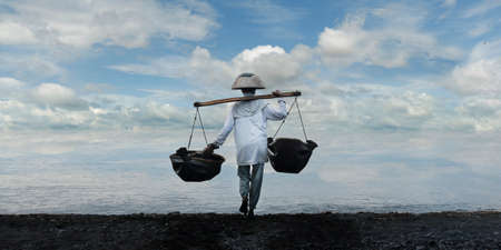 Farmer collecting water in the sea, to salt field for evaporation-Kusamba-Baliの写真素材