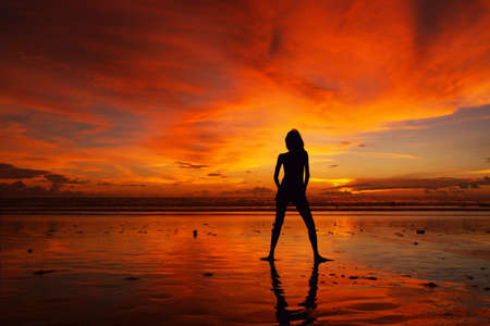 sunset with the silhouette of a model with reflection on the beach in baliの写真素材