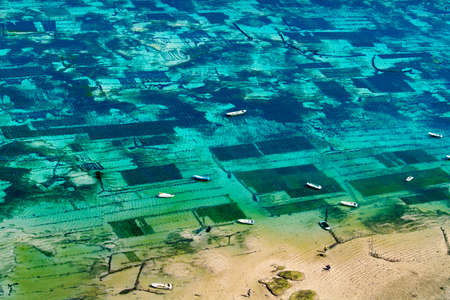 view of the coast with beach and coral at bukit in bali -farmer in boat harvesting sea weed in underwater plantation-indonesiaの写真素材