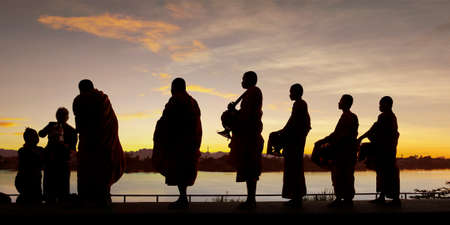 silhouette of monks dressing orange robe during reception of alms, on the shore of the mekong riverの写真素材