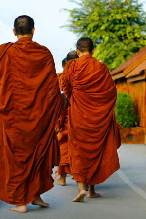 monks dressing orange robe during reception of alms, around buddhist templeの写真素材