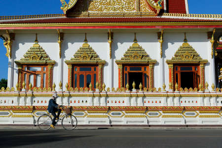 woman ridding bicycle in front of a buddhist temple in thailandのeditorial素材