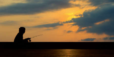 silhouette of fisherman during sunset fishing with fishing rodの写真素材