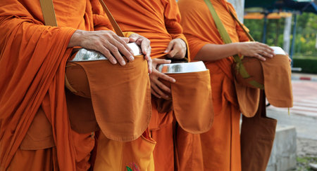 hand of monk dressing orange robe, holding bowl during reception of alms, around buddhist templeの写真素材
