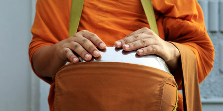 hand of monk dressing orange robe, holding bowl during reception of alms, around buddhist templeの写真素材