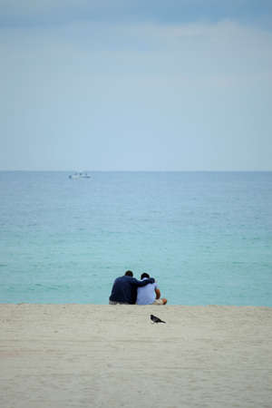Two people sitting on the beach, looking at the endless ocean