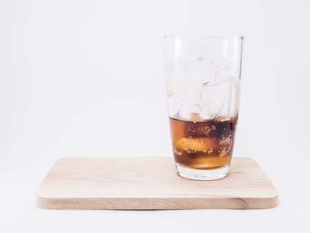 one of thirds soft drink is cool with  two of thirds ice cubes in glass on wood squaresの写真素材