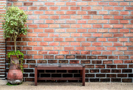 Sidewalk scene with wooden bench and red brick wall.の写真素材