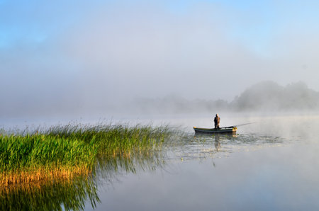 Fisherman on a boat on a misty lake in the morningの写真素材