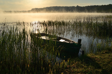 Foggy morning on the lake with fishing boat in the foregroundの写真素材