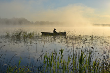 Fishing boat on a foggy lake in the early morning.の写真素材