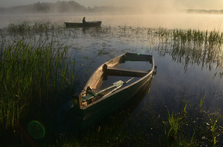Foggy morning on the lake with fishing boat in the foregroundの写真素材