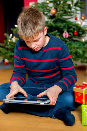 white boy in front of christmas tree with his new tablet pcの写真素材