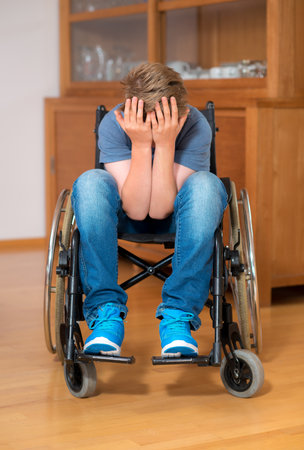 disabled boy in wheelchair at home is sadの写真素材