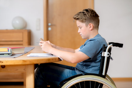 disabled boy in wheelchair doing homework and chatting in the internetの写真素材