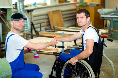 disabled worker in wheelchair in a carpenter's workshop with his colleagueの写真素材