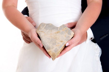 bridal couple holding a stone- heart together in front of white backgroundの写真素材
