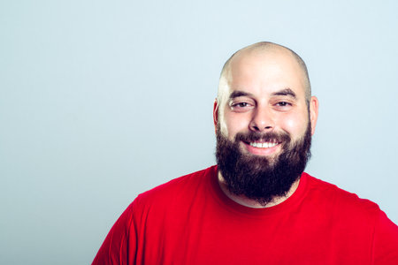 young bearded man in red shirt in front of gray background