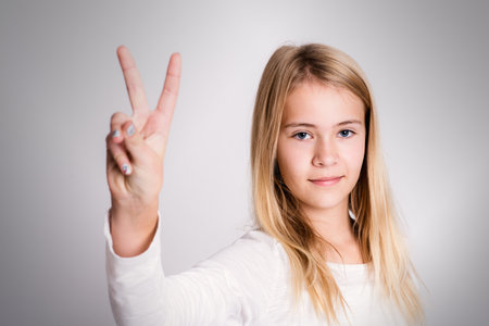 nice blond girl in front of gray background showing victory signの写真素材