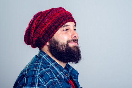 young bearded man with red woolen cap in front of gray backgroundの写真素材