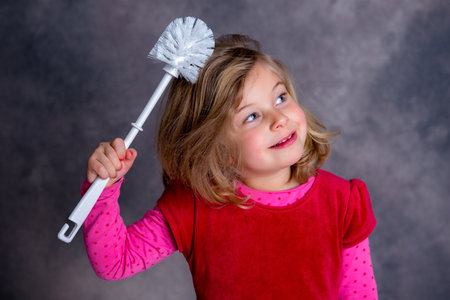 funny girl playing with toilet brush in front of gray backgroundの写真素材