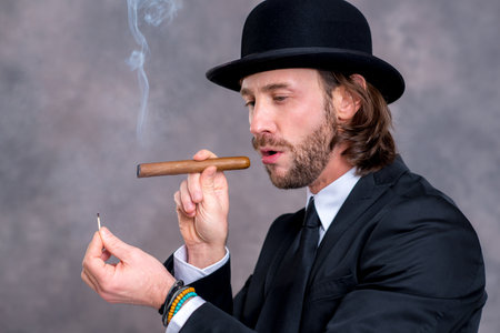 young businessman with bowler hat in black suit smoking big cigarの写真素材