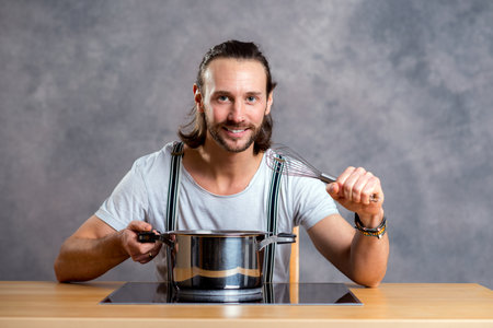 young bearded man with cooking pot in front of gray backgroundの写真素材