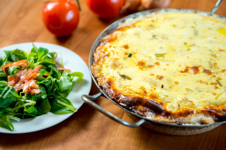 baked quiche with field salad on wooden table