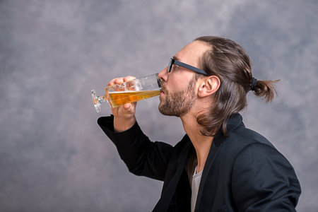 young man in front of gray background drinking beer