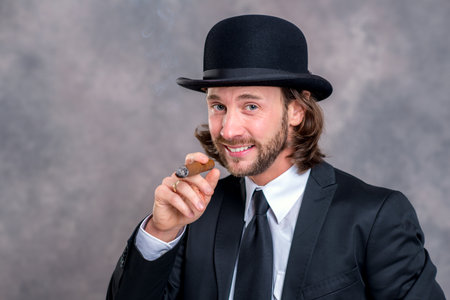 young businessman with bowler hat in black suit smoking big cigarの写真素材