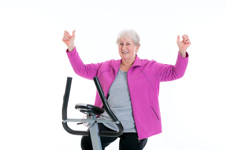 gray-haired female senior with arms up train with fitness machineの写真素材
