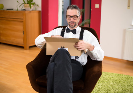 young bearded man in white shirt with bow-tie  opening a packageの写真素材
