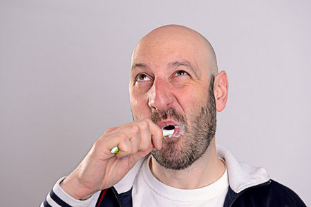 bald headed man brushing teeth in front of gray backgroundの写真素材