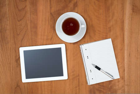 tablet PC, notepad with pen and a cup of tea on wooden table from aboveの写真素材