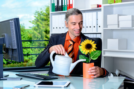 young business man at his desk watering sunflowerの写真素材