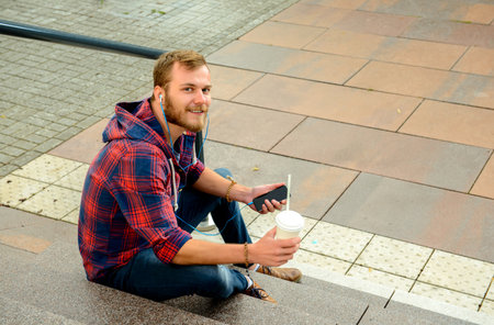 young man with soft drink sitting on stairs and using his smartphoneの写真素材