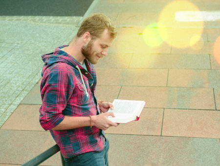 young man with beard standing with book and readingの写真素材