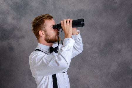 young bearded man in white shirt and bow tie looking through a 	binocularsの写真素材