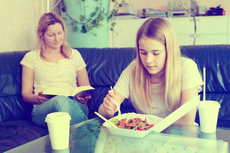 mother reading a book and daughter eating  fast foodの写真素材