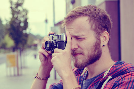young bearded man with old camera standing in front of city background